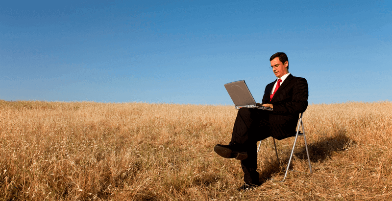 person in a field working on laptop in formal attire